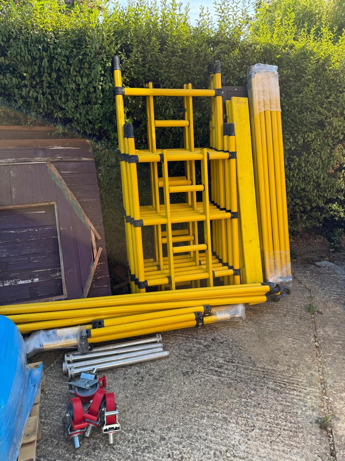 Yellow GRP fibreglass scaffold tower components, frames, braces, platforms and castors ready for assembly.