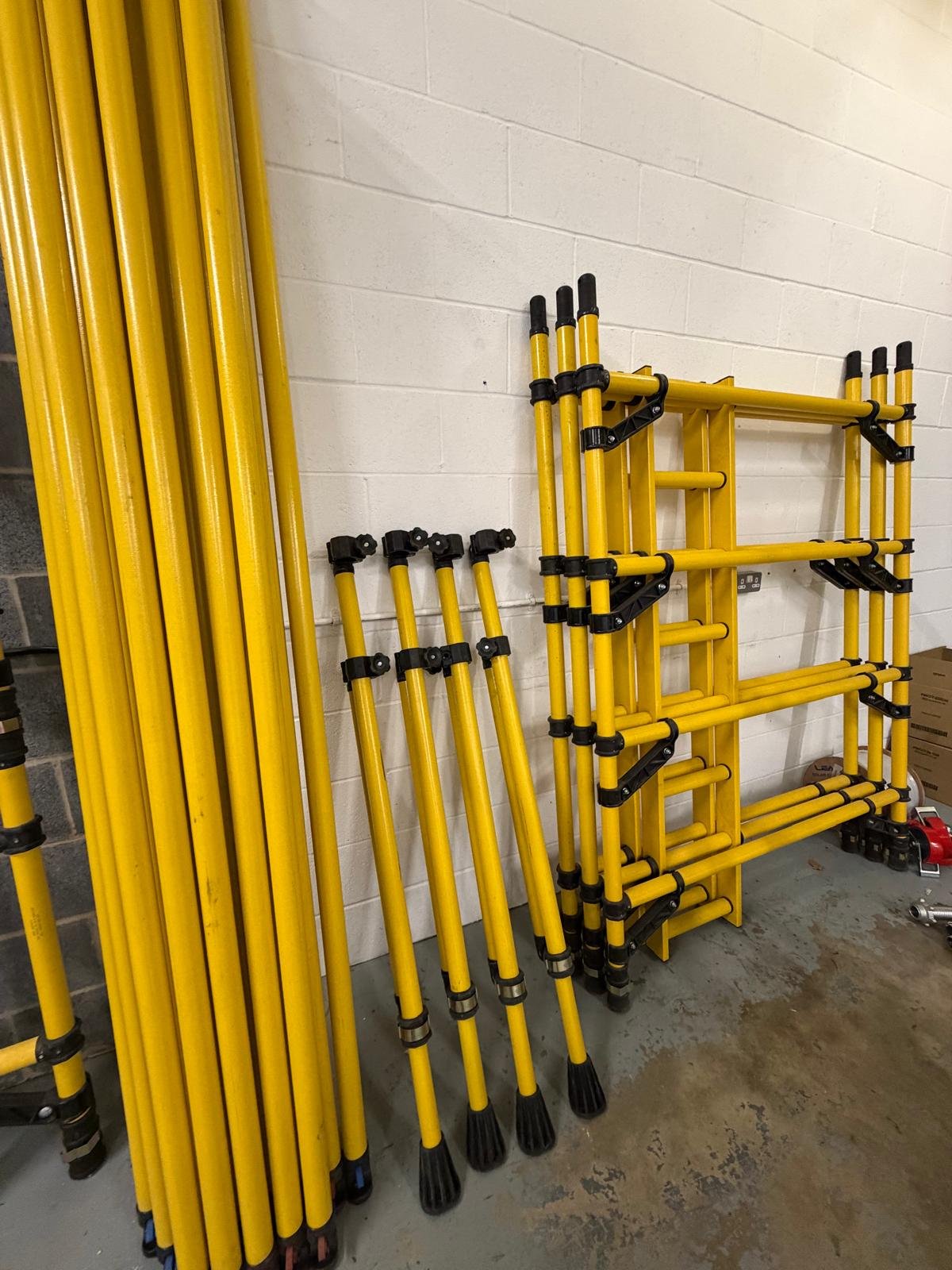 Yellow GRP fibreglass scaffold tower components including frames, braces and stabilisers stored ready for assembly.
