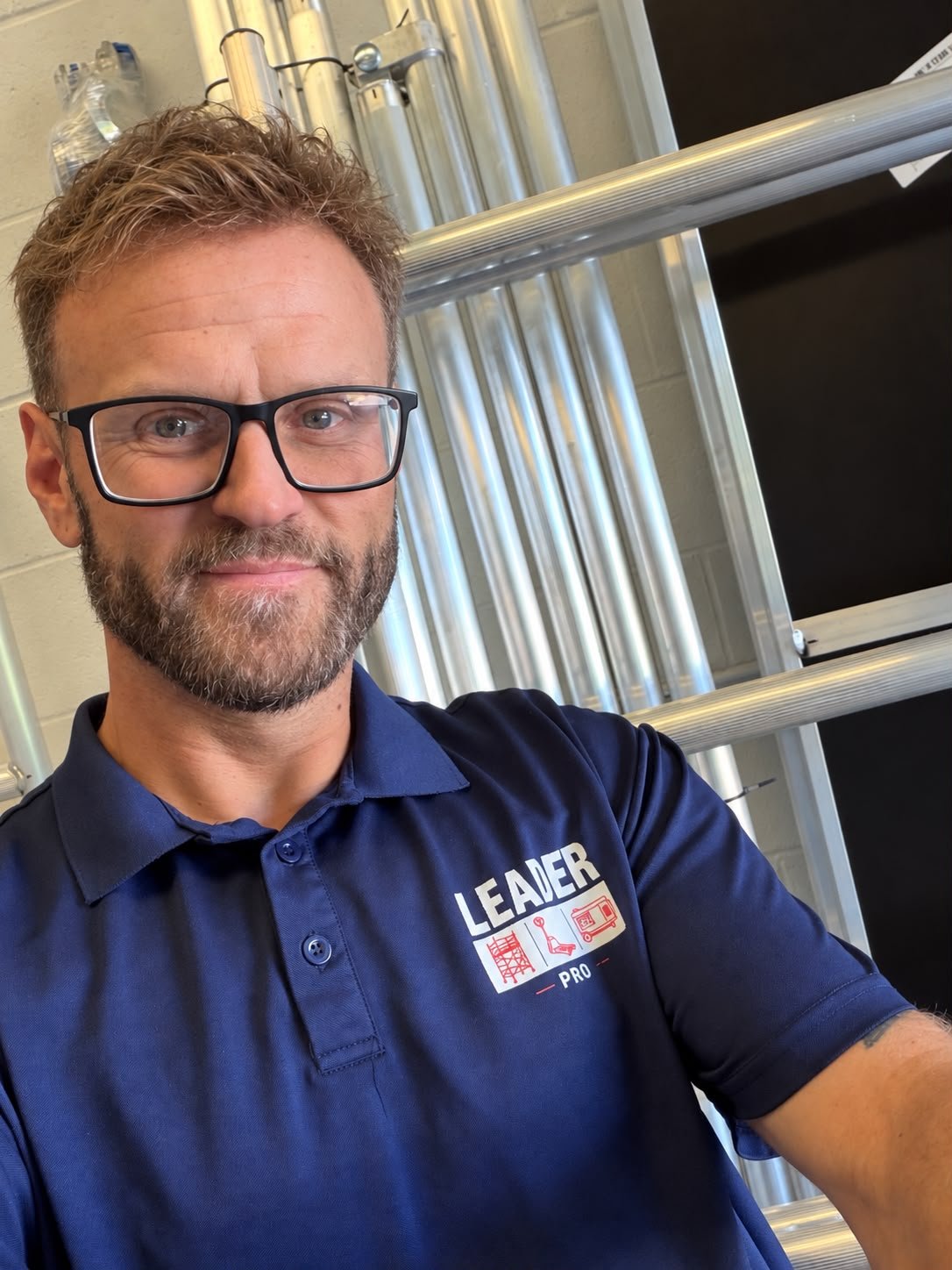 Leader Pro team member wearing branded workwear with aluminium scaffold tower components in the background.